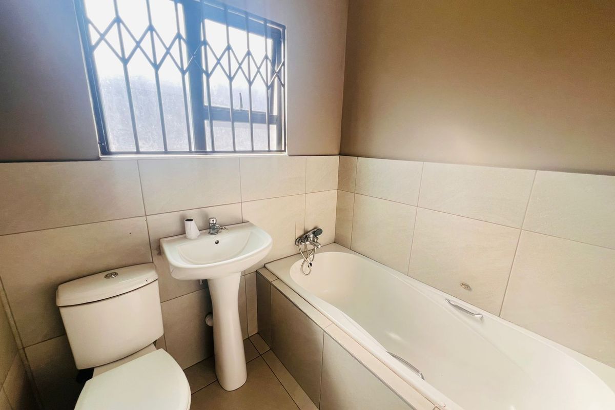 A functional bathroom featuring a pedestal basin, toilet, and bathtub with tiled finishes and a window with security bars.