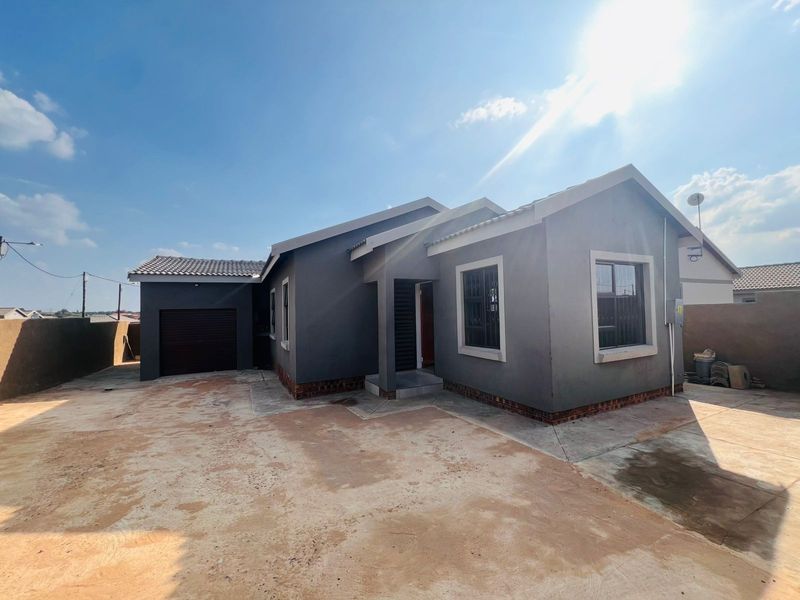 Front elevation of a modern single-story house featuring a grey facade, tiled roof, integrated garage, and a large concrete driveway area.