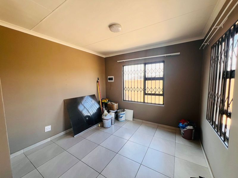 An empty bedroom featuring neutral wall paint, tiled flooring, and windows fitted with security bars.