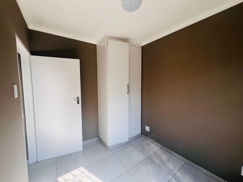 A clean, empty bedroom featuring neutral brown walls, white built-in cupboards, and modern tiled flooring.