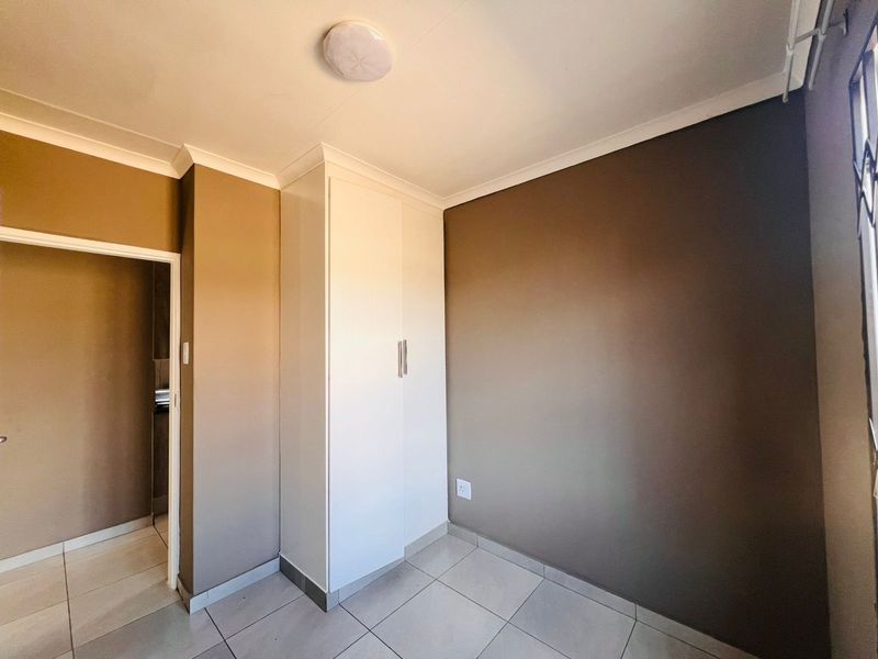 A clean, empty bedroom featuring neutral wall tones, tiled flooring, and a built-in white cupboard, offering a versatile space ready for personalization.