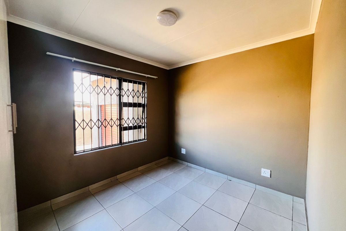 A clean, empty bedroom featuring neutral-toned walls, tiled flooring, and a window fitted with a security gate.