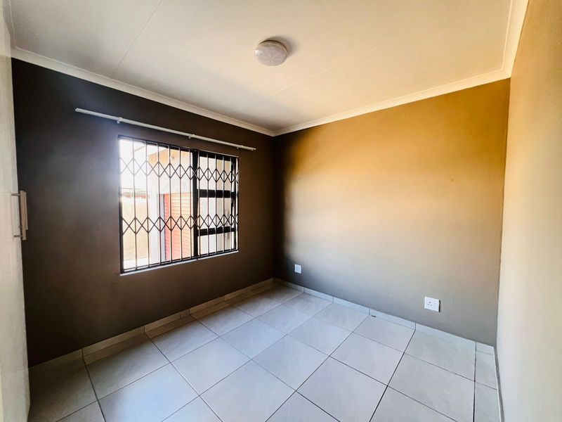A clean, empty bedroom featuring neutral-toned walls, tiled flooring, and a window fitted with a security gate.