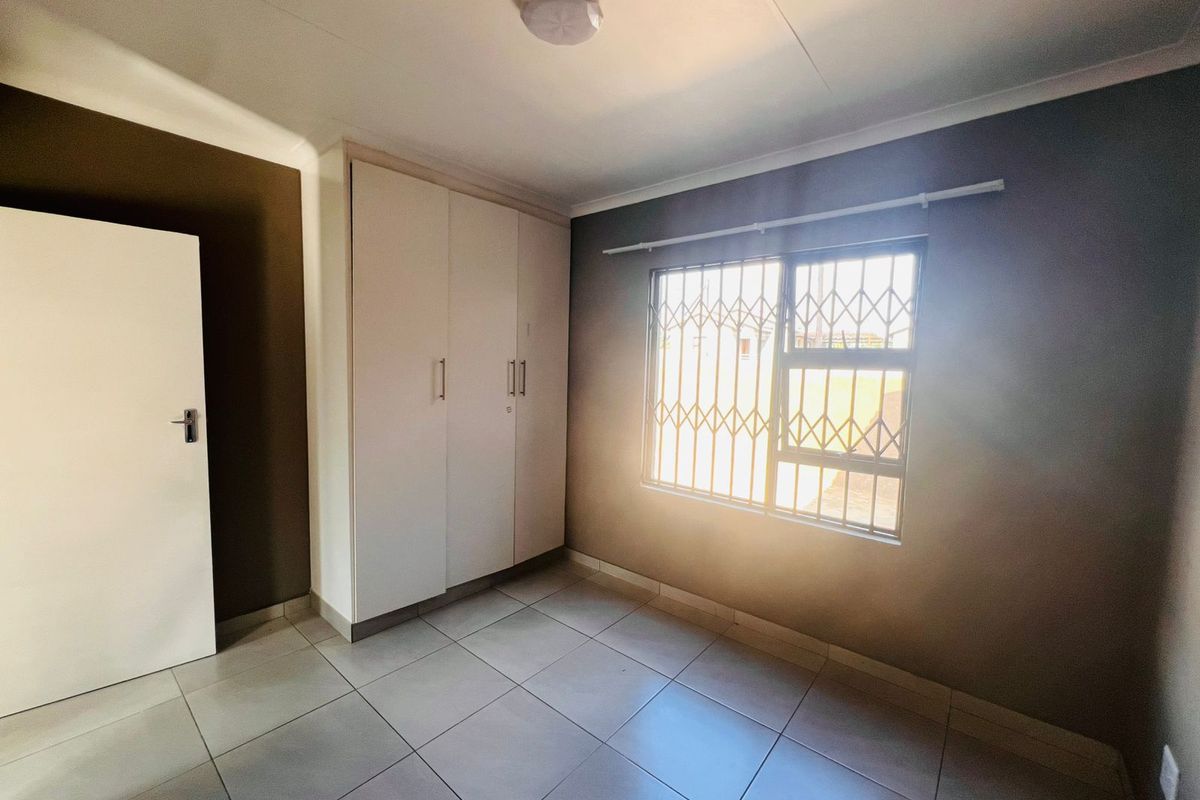 A clean, empty bedroom featuring tiled flooring, built-in cupboards, and a window fitted with a security gate.