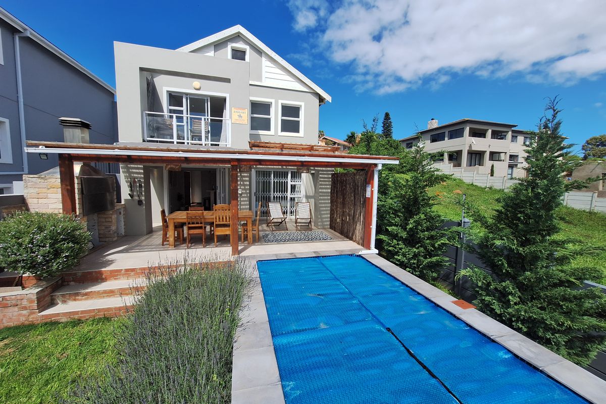 Rear exterior view featuring a covered patio with built-in braai, a swimming pool with cover, and an upper-level balcony.