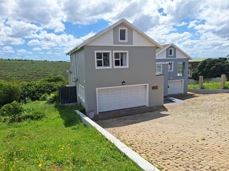 Front elevation of a modern duet property featuring a paved driveway, double garage, and well-maintained exterior finishes set against a natural landscape.
