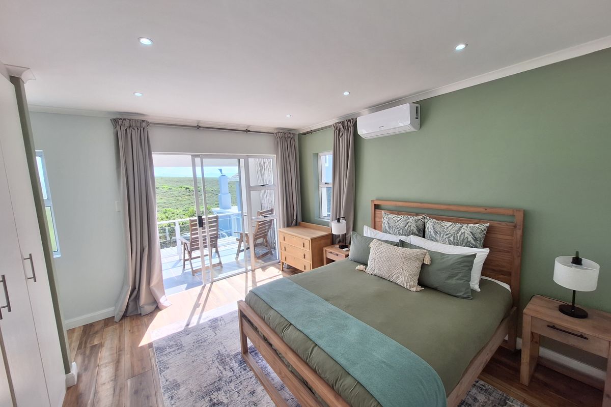 A well-maintained bedroom featuring laminate flooring, built-in cupboards, split-system air conditioning, and a sliding glass door leading to a private balcony with scenic views.