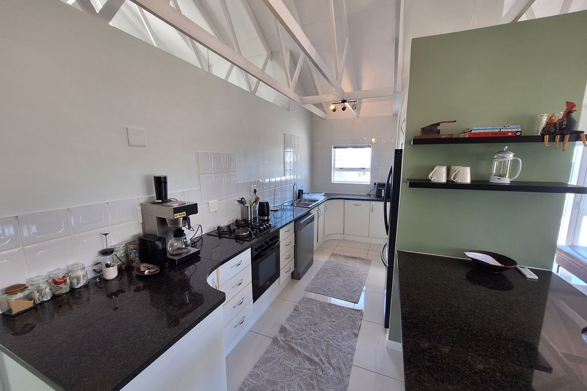 Modern kitchen featuring granite countertops, gas hob, built-in oven, and distinctive exposed roof trusses, offering a functional and well-lit workspace.