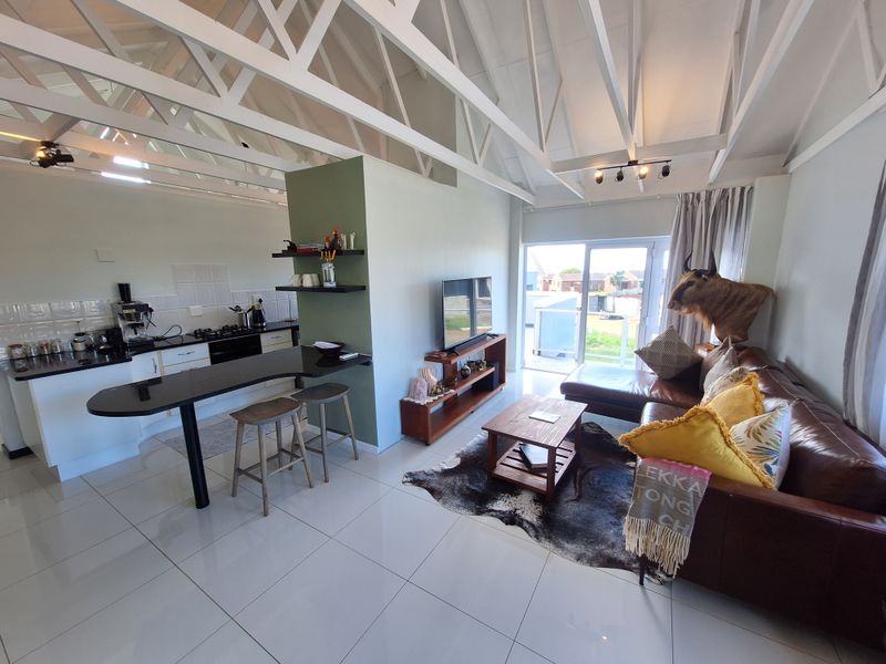Open-plan living area featuring a modern kitchen with granite countertops, breakfast bar, and exposed roof trusses, leading out to a patio through sliding doors.