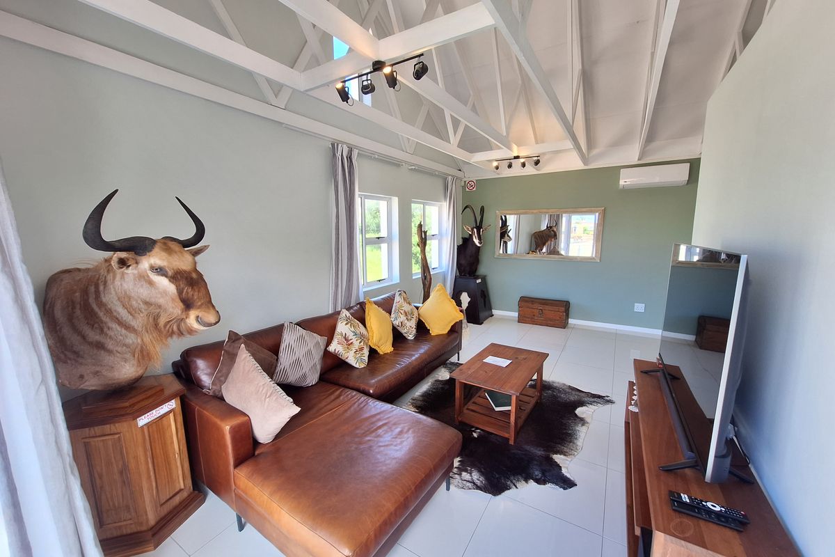Spacious living room featuring high vaulted ceilings with exposed white trusses, tiled flooring, and a wall-mounted air conditioning unit.