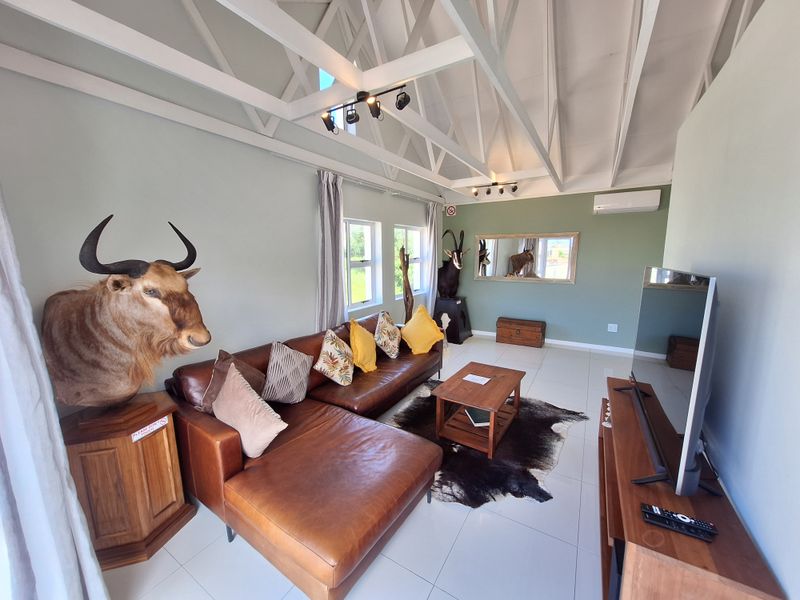 Spacious living room featuring high vaulted ceilings with exposed white trusses, tiled flooring, and a wall-mounted air conditioning unit.