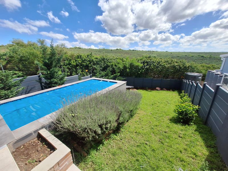 A well-maintained outdoor pool area featuring a swimming pool with a cover, landscaped garden, and secure perimeter fencing with scenic hillside views.