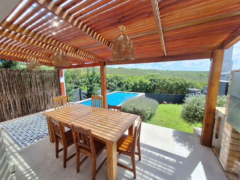 Covered outdoor patio featuring a wooden pergola, tiled flooring, and direct access to a private swimming pool and garden area.