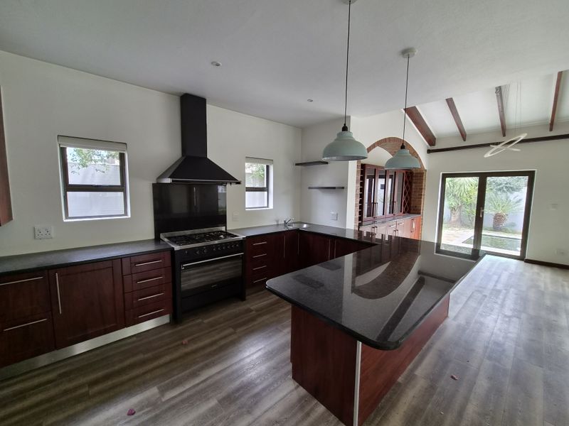 Spacious kitchen featuring dark wood cabinetry, granite countertops, a gas stove with extractor, and a central island, opening onto a patio area.