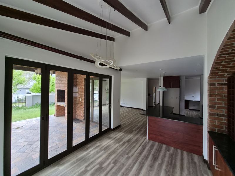 Spacious open-plan living and kitchen area featuring exposed timber beams, modern laminate flooring, and large bi-fold doors opening to an outdoor patio.
