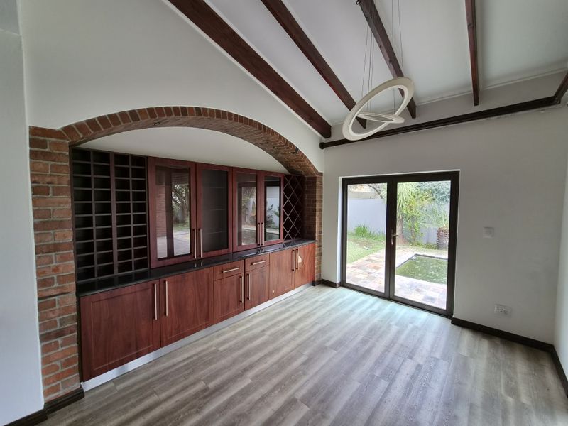 A well-maintained bar area featuring custom built-in cabinetry, wine storage, an exposed brick archway, and timber ceiling beams, with direct access to the garden.