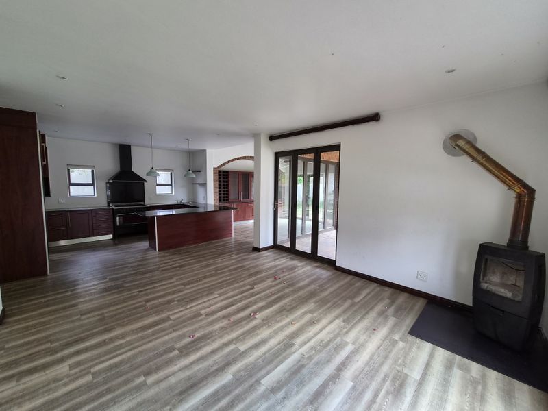 Spacious open-plan living area featuring a wood-burning fireplace, modern laminate flooring, and a well-appointed kitchen with a central island and built-in cabinetry.