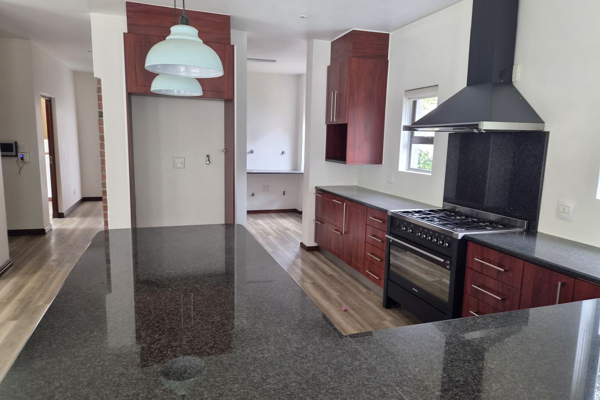 Modern kitchen featuring dark wood cabinetry, granite countertops, a gas stove with extractor fan, and durable laminate flooring in an open-plan layout.