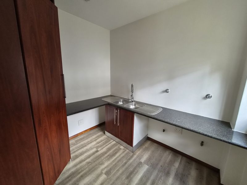 A functional laundry room featuring laminate flooring, granite countertops, a stainless steel sink, and built-in cabinetry with dedicated plumbing connections.
