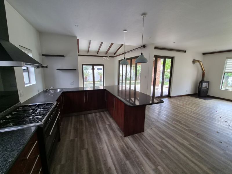 Spacious open-plan kitchen and living area featuring dark wood cabinetry, granite countertops, a wood-burning fireplace, and direct access to the outdoor patio.