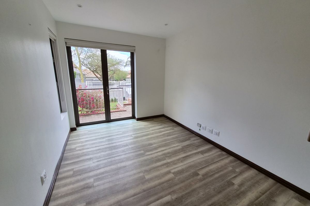 A bright, empty bedroom featuring modern laminate flooring, recessed lighting, and a sliding glass door providing access to an outdoor area.