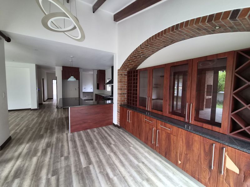 Spacious open-plan living and kitchen area featuring modern laminate flooring, custom wood cabinetry, granite countertops, and a distinctive exposed brick archway.