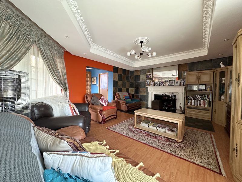 Spacious living room featuring a stone-tiled feature wall, fireplace mantel, ornate ceiling cornicing, and laminate flooring, offering a warm and traditional aesthetic.