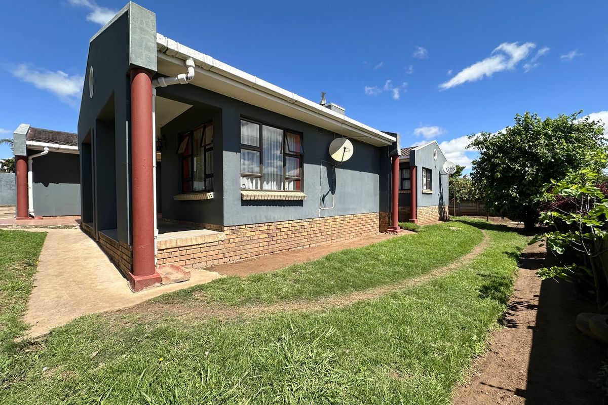 Rear view of the property featuring a covered patio area, brick base detailing, and a surrounding garden with a paved walkway.