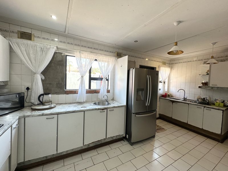 A functional kitchen featuring tiled flooring, laminate countertops, and built-in cabinetry, currently requiring cosmetic updates and repairs to the wall tiling and cabinet bases.
