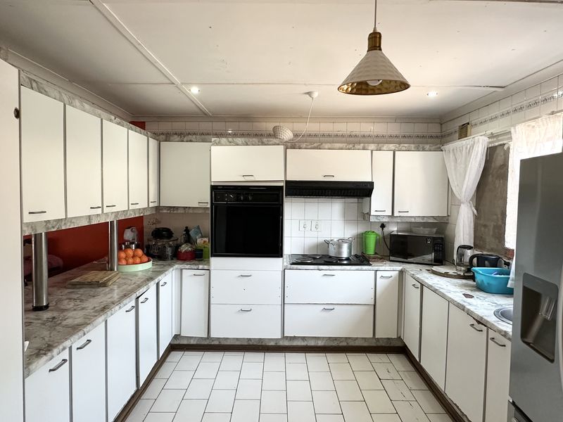 A functional kitchen featuring white cabinetry, laminate countertops, built-in oven, and hob, with tiled flooring and backsplash throughout.