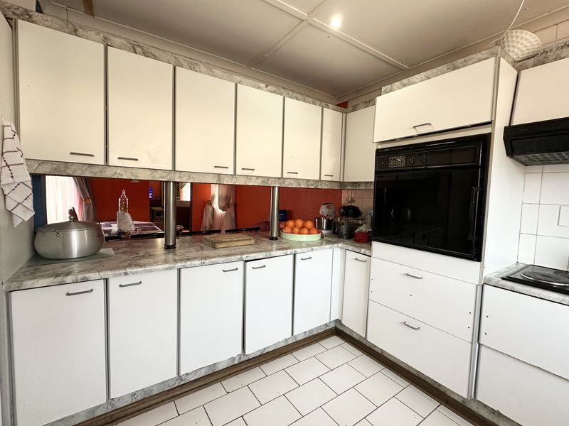 A functional kitchen featuring white cabinetry, built-in oven, extractor fan, and tiled flooring, offering a dated aesthetic ready for modern updates.