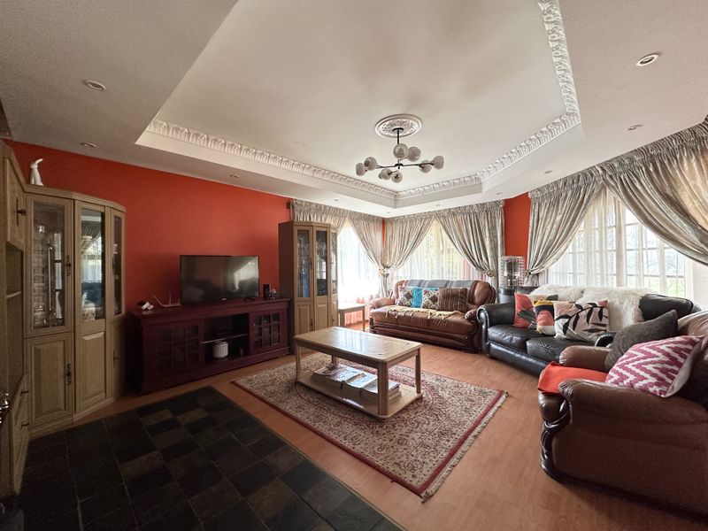 Spacious living room featuring a decorative tray ceiling with recessed lighting, dual-tone flooring with slate and laminate, and large windows with curtain treatments.