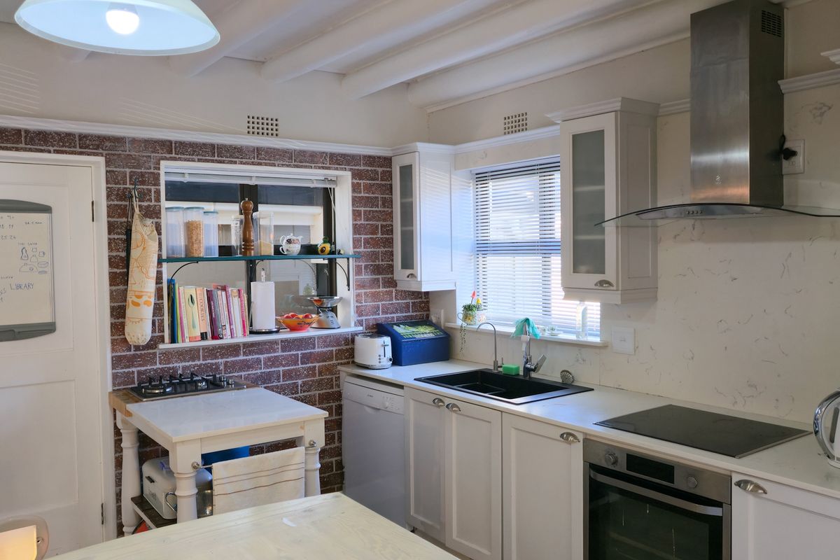 A well-lit kitchen featuring exposed brick walls, white cabinetry, stainless steel appliances, and a marble-look splashback, complemented by exposed ceiling beams.