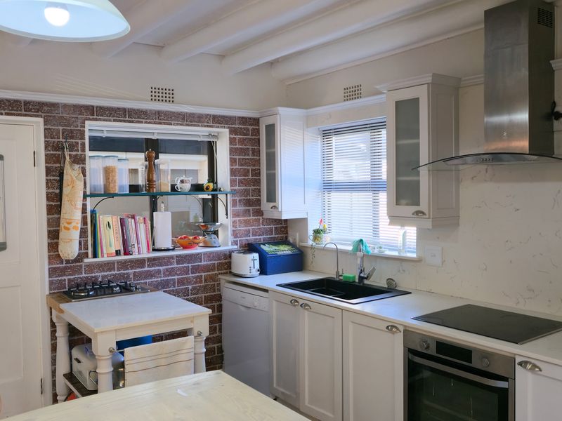 A well-lit kitchen featuring exposed brick walls, white cabinetry, stainless steel appliances, and a marble-look splashback, complemented by exposed ceiling beams.
