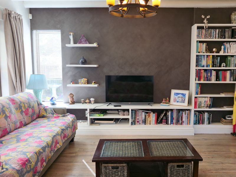 A cozy living room featuring a dark feature wall, built-in white shelving, floating shelves, and durable laminate flooring.