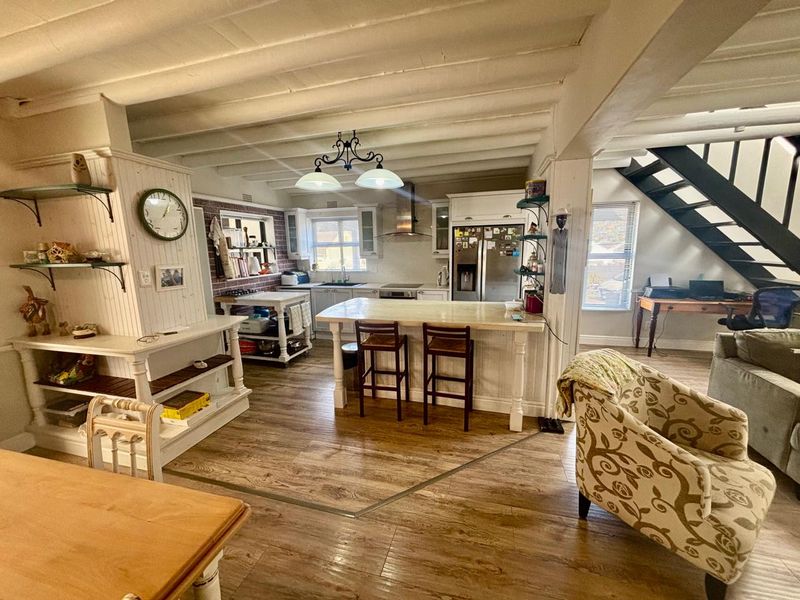 Open-plan living and kitchen area featuring exposed ceiling beams, a central island, and a staircase, creating a functional and character-filled space.