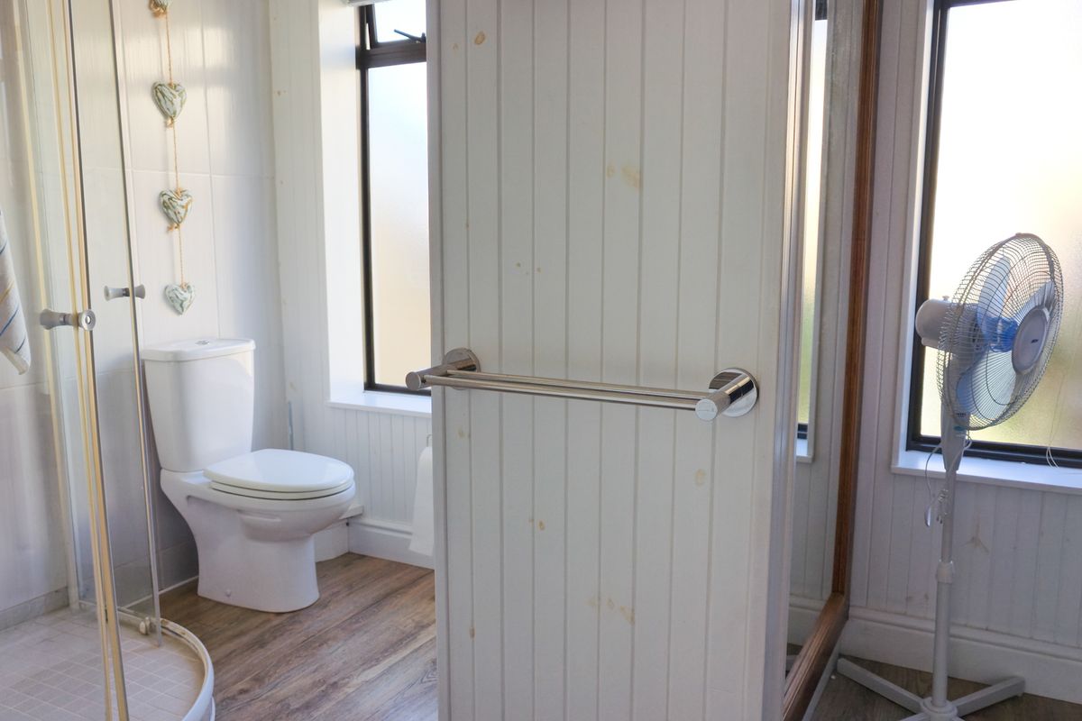 A functional bathroom featuring a shower enclosure, toilet, and tongue and groove wall paneling with wood-look flooring.