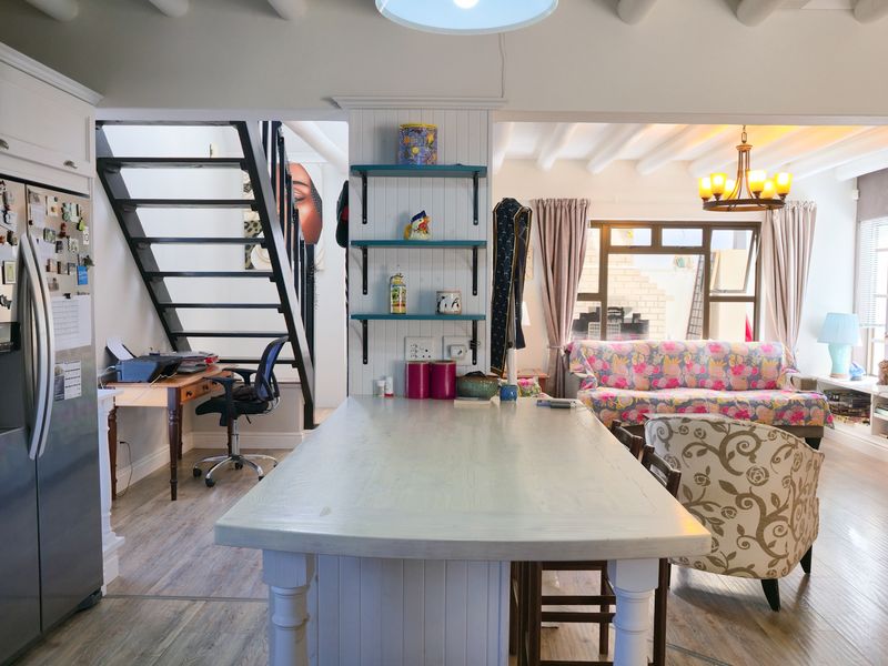 Open-plan living area featuring a central kitchen island, exposed ceiling beams, and a staircase, creating a functional and connected multi-purpose space.