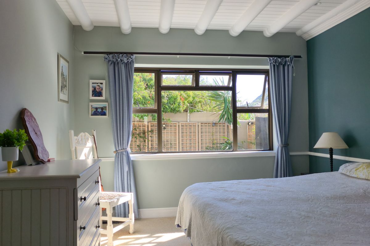 A well-maintained bedroom featuring exposed beam ceilings, a chair rail, and a large casement window overlooking the rear garden.