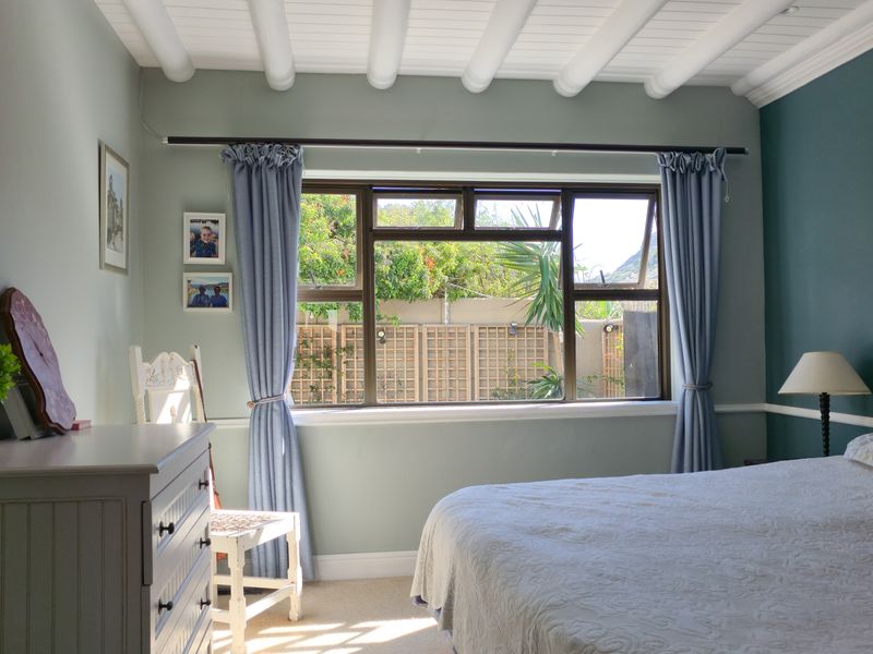 A well-maintained bedroom featuring exposed beam ceilings, a chair rail, and a large casement window overlooking the rear garden.