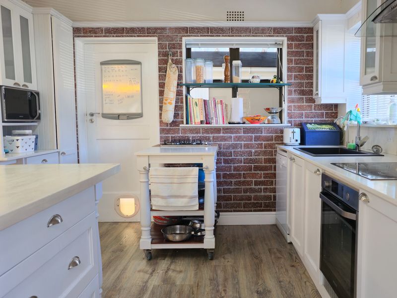 A well-lit kitchen featuring white cabinetry, an exposed brick feature wall, integrated appliances, and durable laminate flooring.