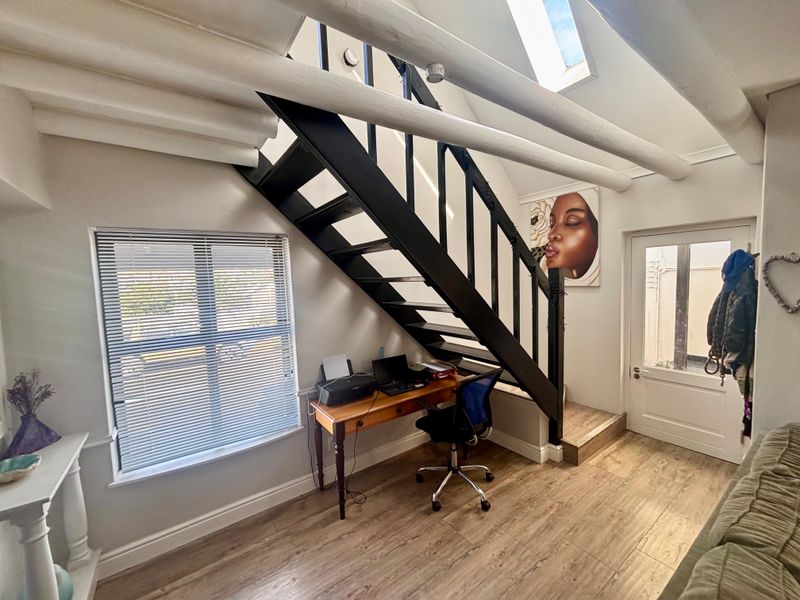 A bright living area featuring exposed timber ceiling beams, a skylight, laminate flooring, and a striking black staircase leading to an upper level.