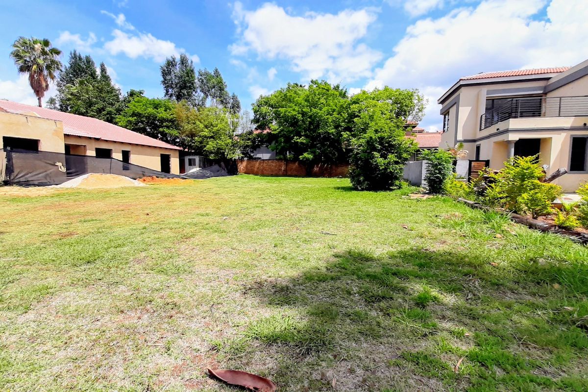 A spacious residential plot featuring a well-maintained lawn, established trees, and boundary walls, offering a clear view of adjacent residential structures.