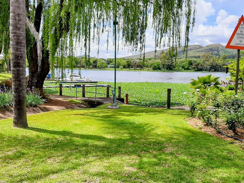 A scenic view of a tranquil lakefront area featuring a well-maintained lawn, mature trees, and direct access to the water.
