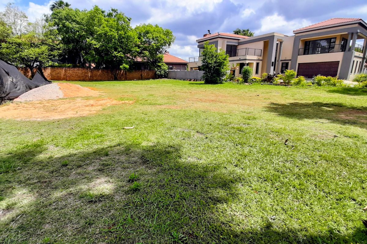 A spacious, well-maintained residential garden featuring a large lawn area, mature trees, and a secure perimeter wall.