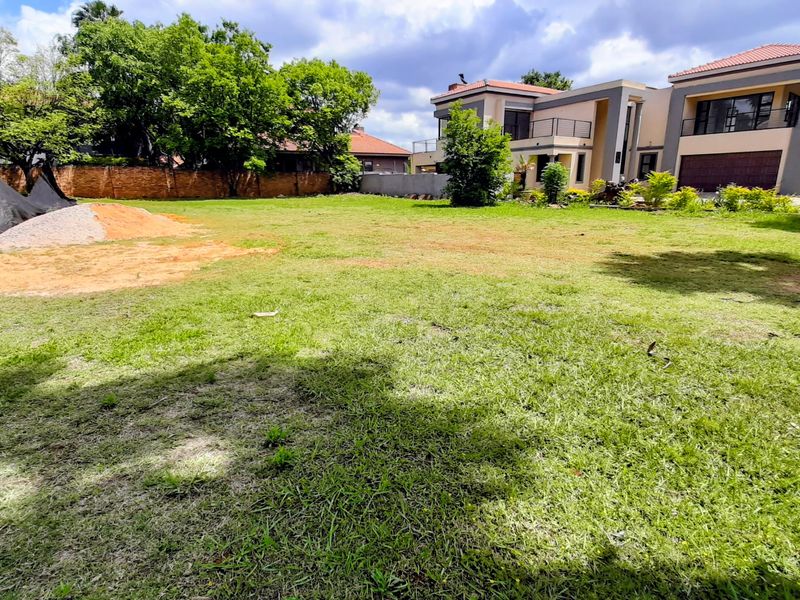 A spacious, well-maintained residential garden featuring a large lawn area, mature trees, and a secure perimeter wall.