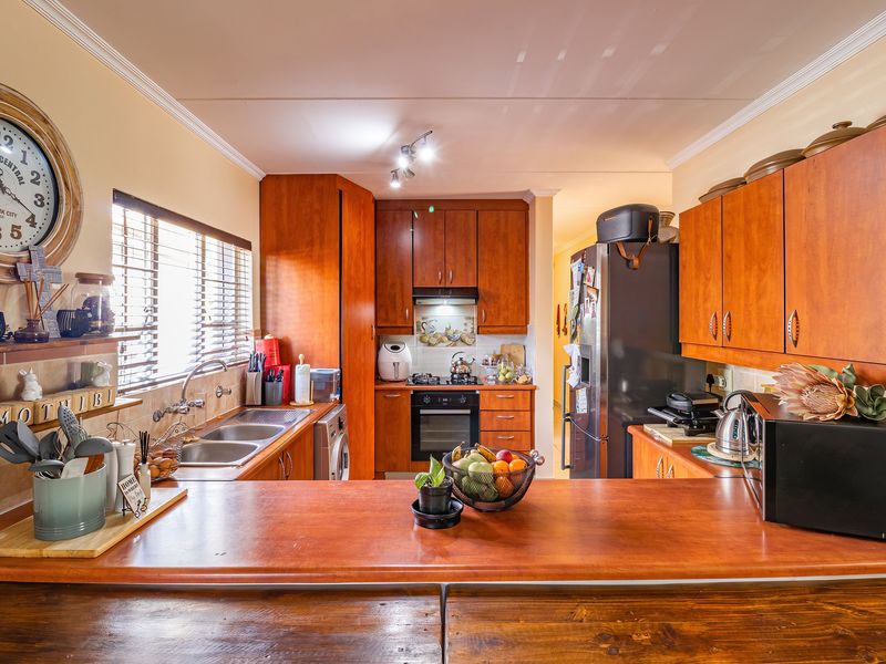 A functional kitchen featuring warm-toned wooden cabinetry, laminate countertops, a double stainless steel sink, and built-in cooking appliances with a tiled backsplash.