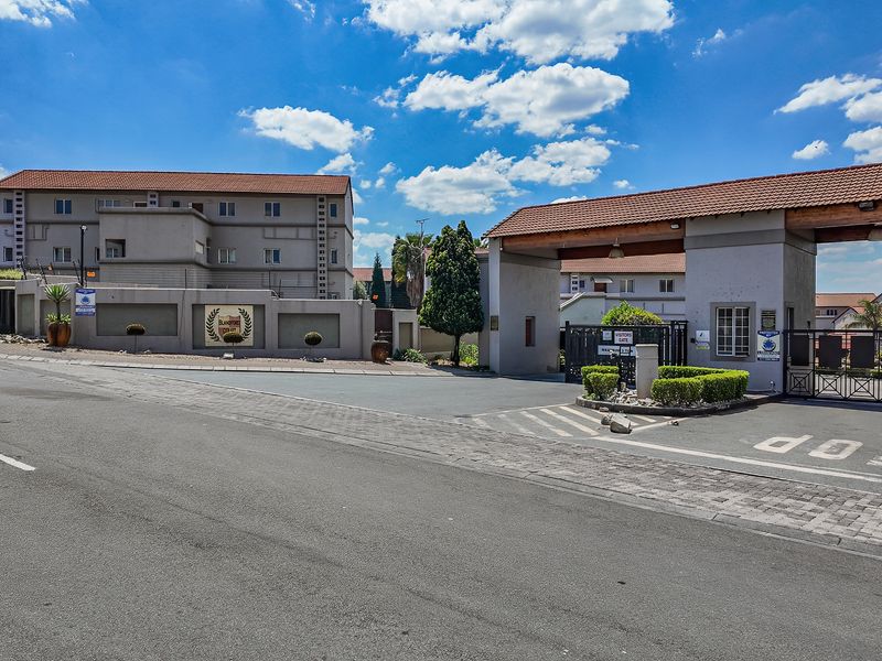 Street view of the secure apartment complex entrance featuring a gated access point, perimeter walling, and well-maintained exterior building facades.