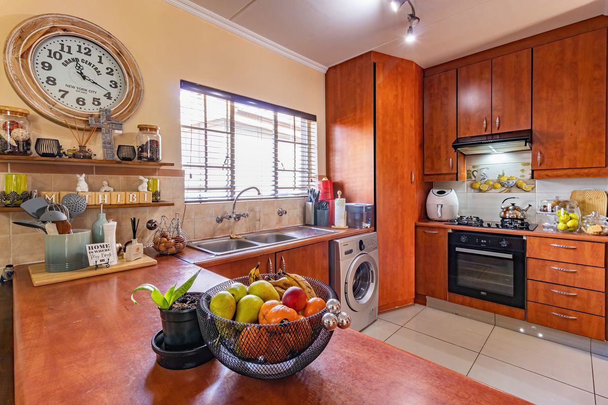 A functional kitchen featuring warm-toned wooden cabinetry, a double basin sink, built-in oven with gas hob, and tiled flooring with a decorative backsplash.