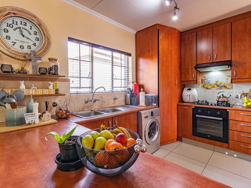 A functional kitchen featuring warm-toned wooden cabinetry, a double basin sink, built-in oven with gas hob, and tiled flooring with a decorative backsplash.